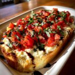 A slice of toasted bread topped with creamy cheese, fresh tomato bruschetta topping, and balsamic glaze, perfect for bruschetta dip.