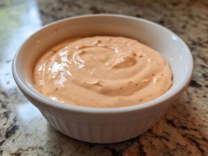 A close-up shot of creamy, pinkish-orange burger sauce swirled in a small white ramekin.