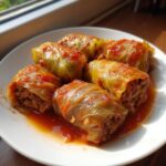Close-up of five savory cabbage rolls stuffed with meat and covered in a rich tomato sauce on a white plate.