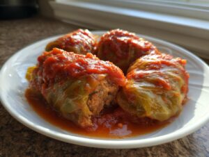 Four savory cabbage rolls generously topped with bright red tomato sauce, served on a white plate.