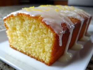 A moist slice of bright yellow lemon pound cake topped with thick white glaze and lemon zest.