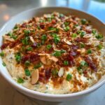 A creamy bowl of amazing Neiman Marcus dip topped with bacon, sliced almonds, and green onions.