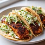 Three delicious salmon tacos filled with blackened seasoned salmon and creamy slaw on a white plate.