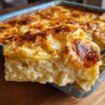 A rich, creamy slice being lifted from a baking dish of amazing scalloped potatoes recipe with a golden-brown, cheesy crust.