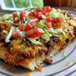 A close-up shot of a thick slice of amazing taco pizza topped with seasoned ground beef, melted cheese, lettuce, and diced tomatoes.