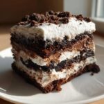 Close-up of a rich, layered brownie refrigerator cake slice with chocolate, cream, and crumb topping.