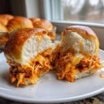 Close-up of buffalo chicken sliders cut in half, showing shredded spicy chicken and melted cheese inside soft rolls.