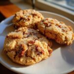 Three golden brown butter pecan cookies, studded with nuts and sprinkled with coarse sugar, resting on a light plate.