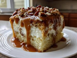 Close-up of a slice of butter pecan praline poke cake dripping with caramel sauce and topped with pecans.