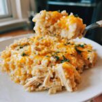 A spoonful of creamy, cheesy chicken and rice being lifted from a plate of the comfort dish.