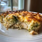 A close-up serving of a creamy chicken and broccoli rice casserole with a golden, melted cheese topping.