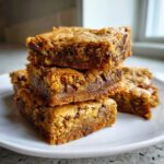 A stack of four rich, chewy chocolate chip cake mix cookie bars piled on a white plate.