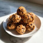 A stack of homemade chocolate chip protein balls made with oats, sitting on a white plate in bright sunlight.
