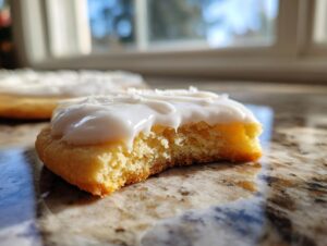 Close-up of a bitten sugar cookie topped with thick, white, glossy cookie icing recipe, set on a granite counter.