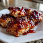 Close-up of perfectly cooked cranberry chicken pieces glazed with a rich, dark red cranberry sauce.
