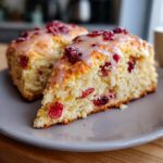 Close-up of two delicious cranberry orange scones topped with a sweet citrus glaze on a gray plate.