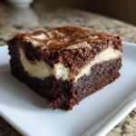 A single square of rich, fudgy cream cheese brownies showing a distinct white cream cheese swirl layer.