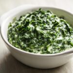 Close-up of rich, dark green creamed spinach recipe served hot in a white ceramic bowl.