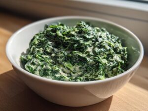 A close-up of a white bowl filled with rich, green creamed spinach recipe, brightly lit.