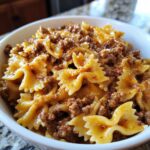 Close-up of a white bowl filled with creamy beef pasta featuring farfalle (bowtie) noodles and ground meat sauce.