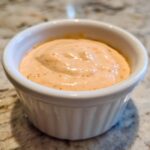 Close-up of creamy, orange-hued burger sauce served in a small white ramekin.