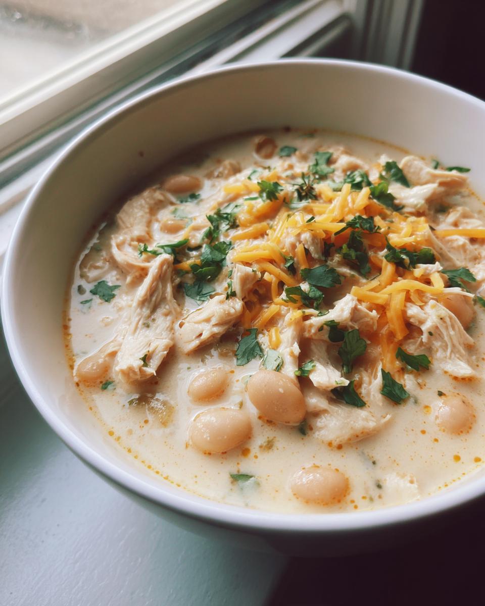 Close-up of a bowl of creamy white chicken chili recipe topped with shredded cheese and cilantro.