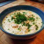 Close-up of a creamy chicken and rice soup, topped generously with fresh parsley.