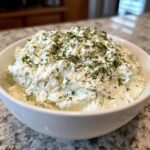 A white bowl filled with creamy dill dip generously topped with fresh chopped dill.