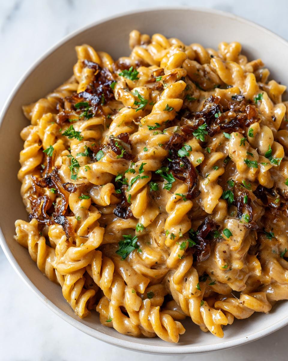 Close-up of creamy French onion pasta made with rotini, topped with dark caramelized onions and fresh parsley.