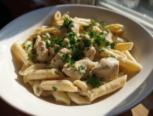 A close-up of creamy garlic parmesan chicken pasta with penne, topped with fresh parsley in a white bowl.