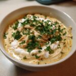 Close-up of a bowl of creamy keto white chicken chili topped with shredded chicken, sour cream, and fresh parsley.