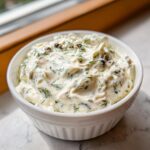 Close-up of creamy homemade tartar sauce garnished with fresh dill and capers in a white bowl.