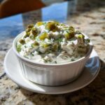 A close-up of creamy homemade tartar sauce recipe topped with chopped pickles, served in a white bowl.