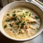 A creamy bowl of white chicken chili recipe, topped with shredded cheese and fresh cilantro.