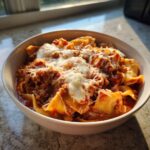 A close-up of a white bowl filled with rich crockpot lasagna soup topped generously with melted mozzarella cheese.