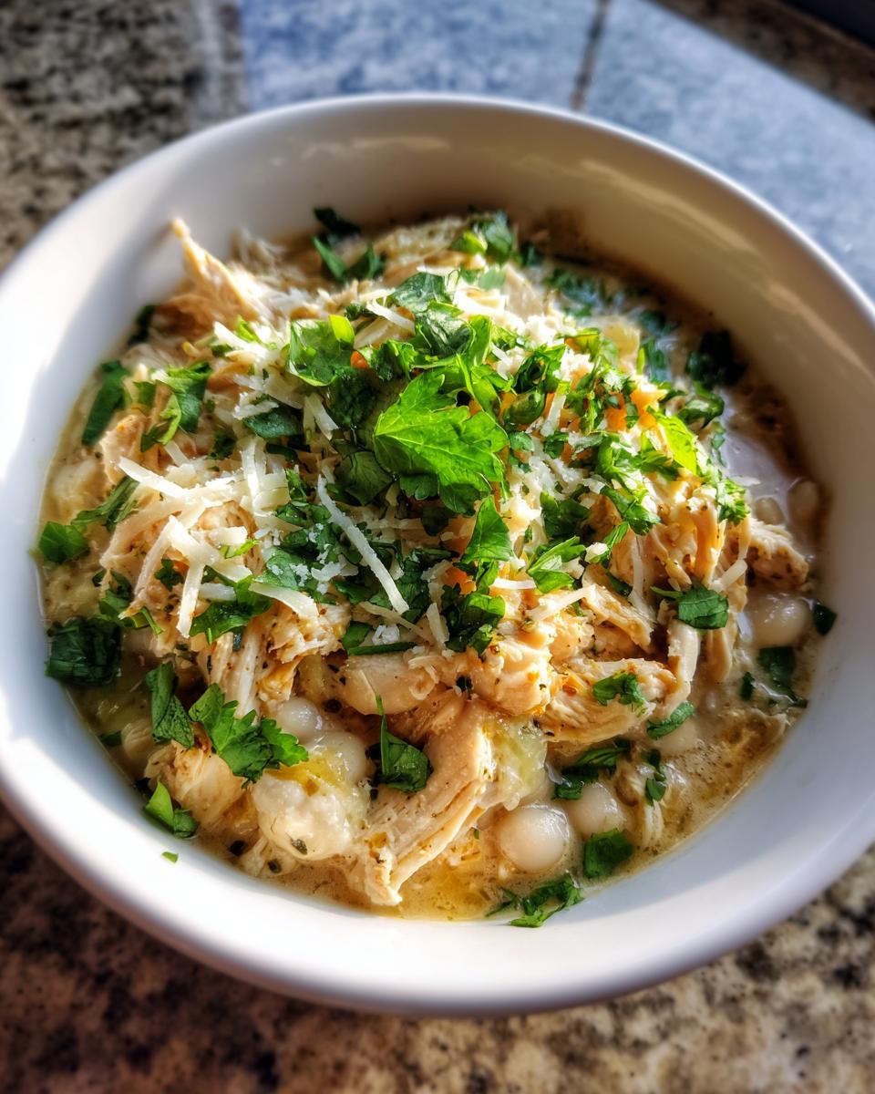 Close-up of a bowl of creamy crockpot white chicken chili topped with shredded cheese and fresh cilantro.