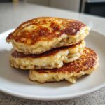 A close-up stack of three golden-brown, fluffy banana pancakes served on a white plate.