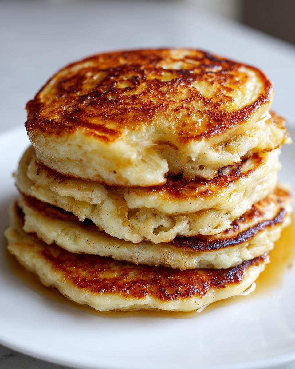 Close-up of a tall stack of fluffy banana pancakes drizzled with syrup on a white plate.