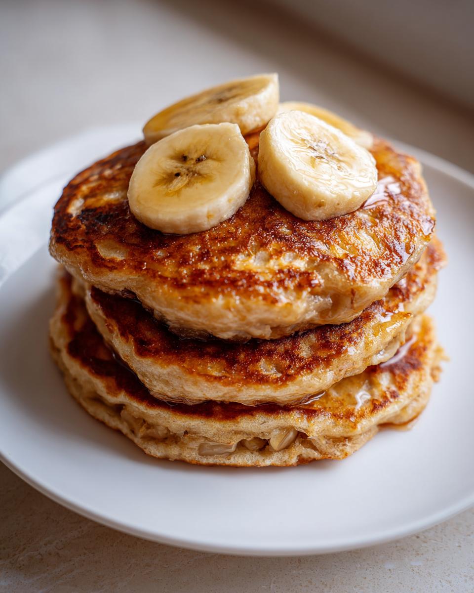 Close-up of a stack of fluffy banana pancakes drizzled with syrup and topped with fresh banana slices.
