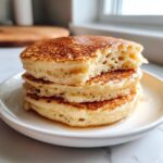 Close-up of a stack of three fluffy coconut flour pancakes drizzled with syrup.