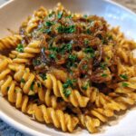Close-up of a serving of french onion pasta made with rotini noodles, topped with rich caramelized onions and fresh parsley.