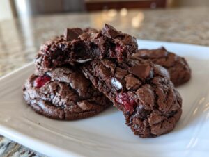Close-up of fudgy chocolate cherry cookies, one broken open revealing a cherry filling.