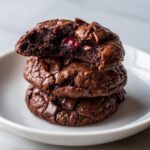 A stack of three fudgy chocolate cherry cookies, showing the soft interior and melted chocolate chips.