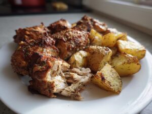 Close-up of baked garlic parmesan chicken and potatoes served on a white plate, showing shredded chicken texture.