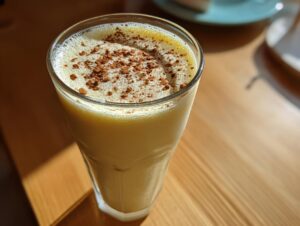 Close-up of a tall glass filled with creamy homemade eggnog, topped with a dusting of cinnamon or cocoa.