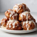 A tempting stack of golden brown apple fritter bites drizzled heavily with white vanilla glaze.