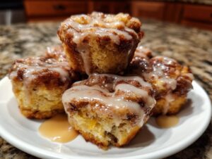 A close-up of several glazed baked apple fritters stacked on a white plate, drizzled with icing.