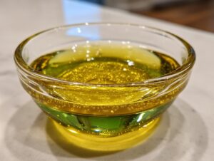 Close-up of golden, slightly bubbly oil in a small glass bowl, likely an ingredient for homemade salad dressing.