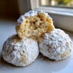 A stack of three gooey butter cookies, heavily dusted with powdered sugar, with one cookie broken open showing the soft interior.