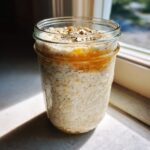A mason jar filled with creamy overnight oats, topped with a layer of honey and seeds.